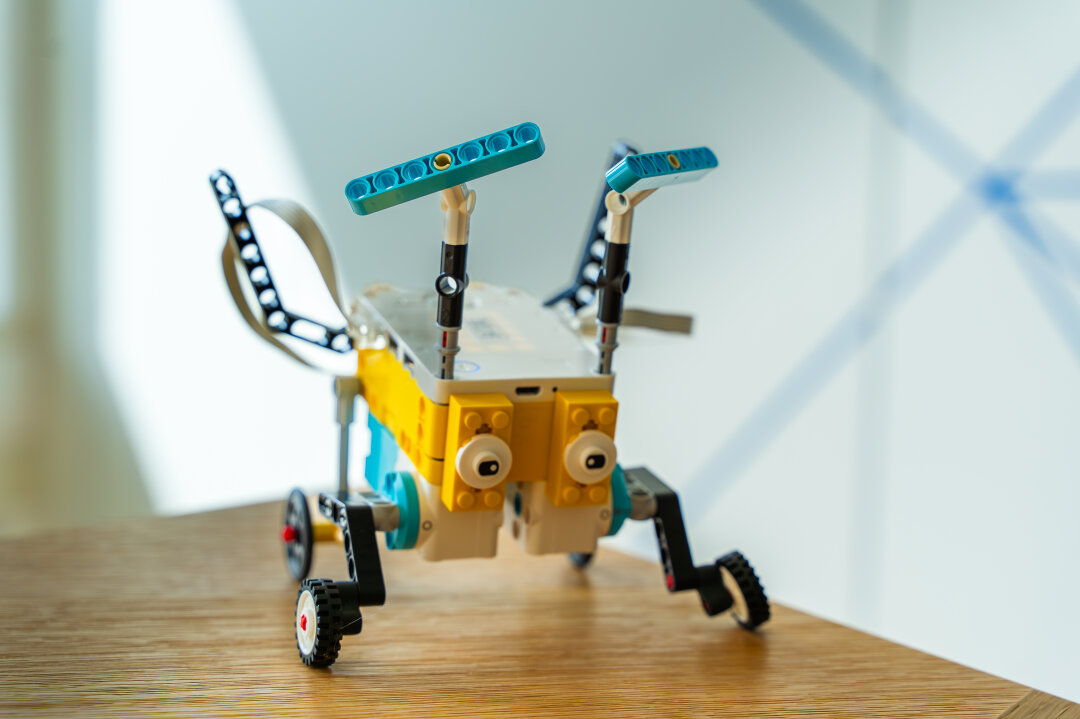 Ein Legoroboter mit Fühlern, der an einen Heuhüpfer erinnern soll. Der Programmierblock bildet den Körper, blaue schmale Klemmblausteine die Fühler. 